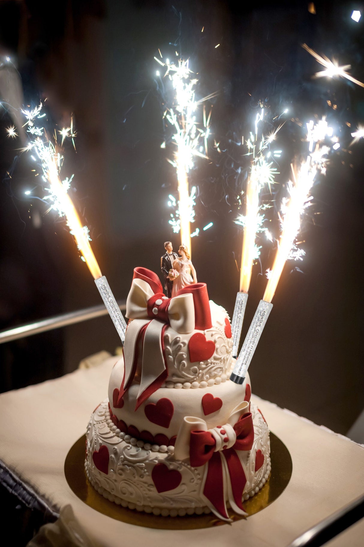 Silver Ice Fountain candles sparkling on a decorated two-tiered heart-themed cake with a bride and groom topper