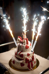 Silver Ice Fountain candles sparkling on a decorated two-tiered heart-themed cake with a bride and groom topper