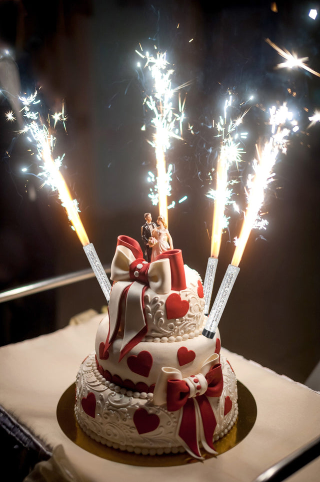 Silver Ice Fountain candles sparkling on a decorated two-tiered heart-themed cake with a bride and groom topper
