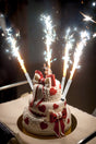 Silver Ice Fountain candles sparkling on a decorated two-tiered heart-themed cake with a bride and groom topper